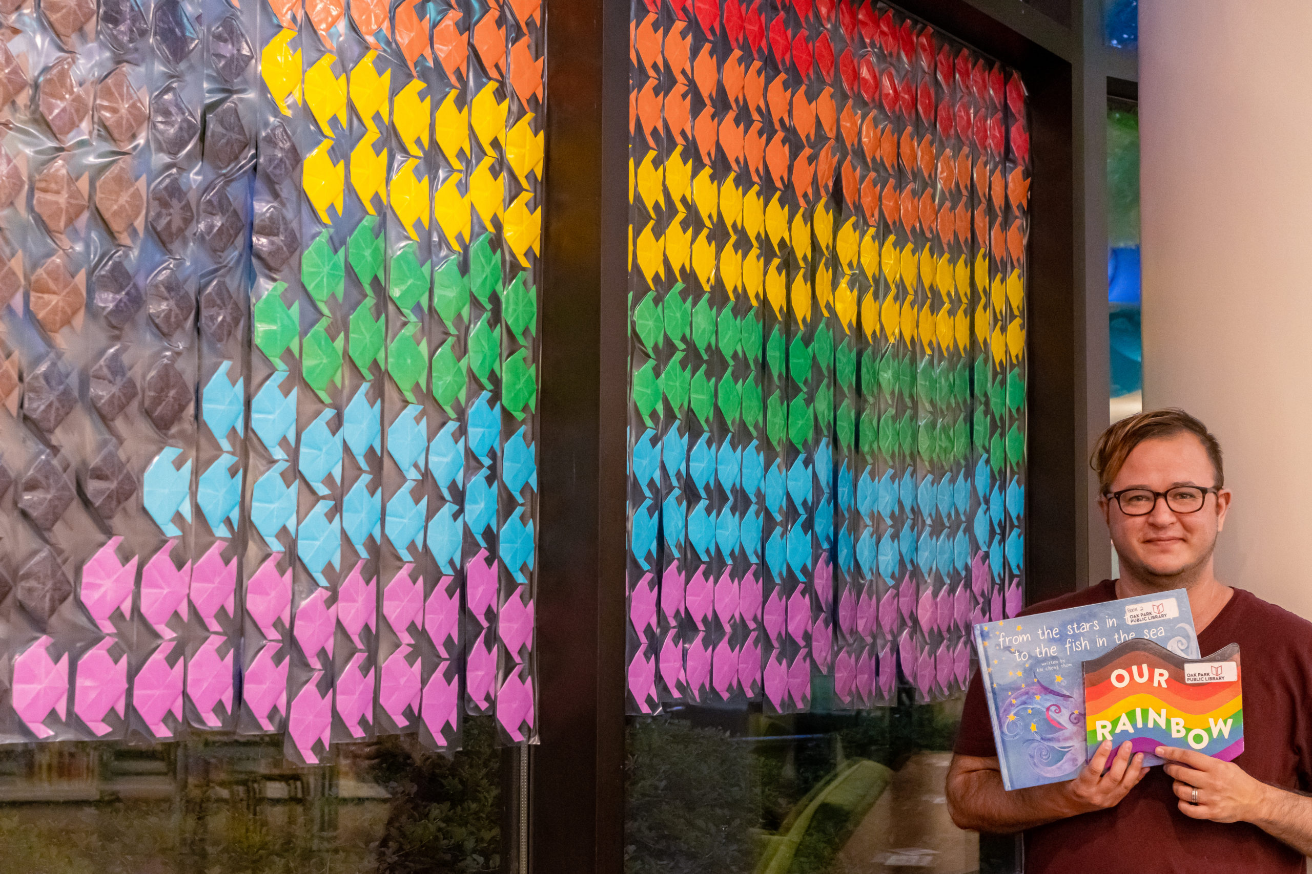 A person with glasses stands in front of a wall of rainbow fish.